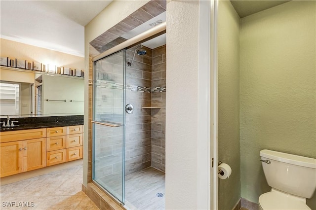 bathroom with a textured wall, tile patterned flooring, toilet, vanity, and a shower stall