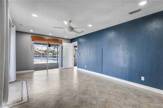 spare room featuring a ceiling fan, visible vents, a textured wall, and baseboards