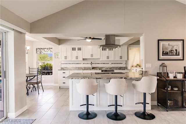 kitchen with light stone counters, island range hood, vaulted ceiling, white cabinetry, and kitchen peninsula