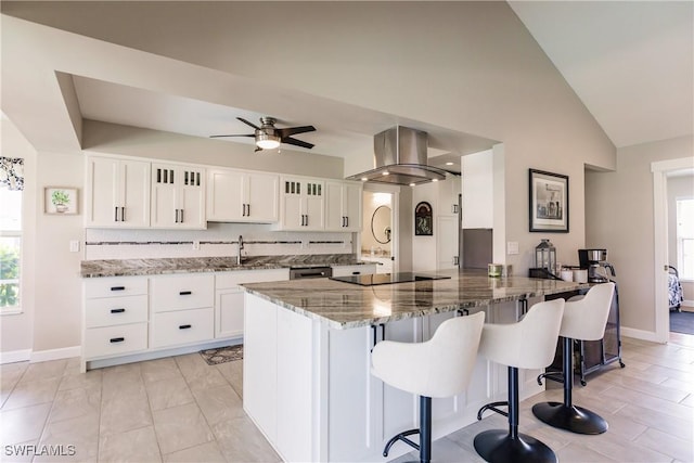 kitchen with light stone counters, island exhaust hood, black electric cooktop, white cabinetry, and kitchen peninsula