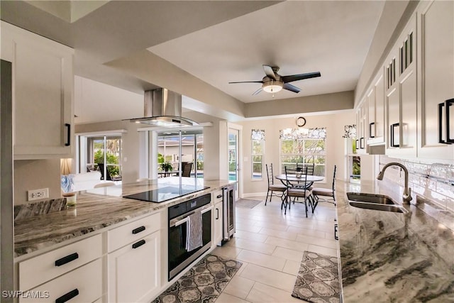 kitchen featuring sink, oven, light stone counters, white cabinets, and island exhaust hood