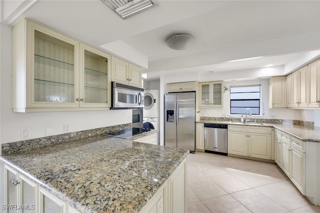 kitchen with glass insert cabinets, appliances with stainless steel finishes, stacked washer / drying machine, a peninsula, and a sink