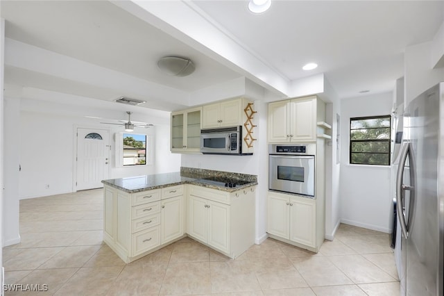 kitchen featuring a wealth of natural light, cream cabinets, appliances with stainless steel finishes, glass insert cabinets, and dark stone countertops