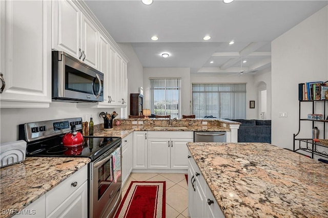 kitchen with light tile patterned floors, arched walkways, white cabinets, appliances with stainless steel finishes, and a sink