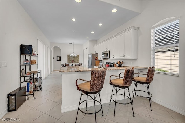 kitchen featuring arched walkways, light tile patterned floors, a peninsula, white cabinets, and appliances with stainless steel finishes