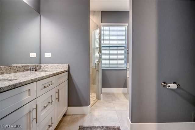 full bath with a sink, baseboards, tile patterned floors, double vanity, and a stall shower