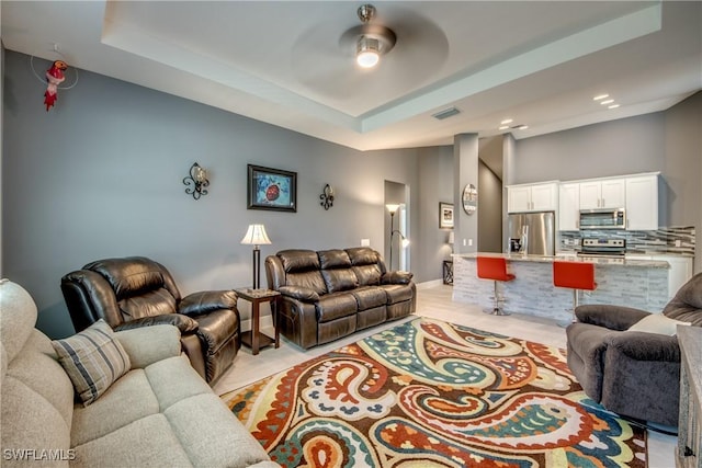 living area featuring a ceiling fan, a tray ceiling, visible vents, and baseboards