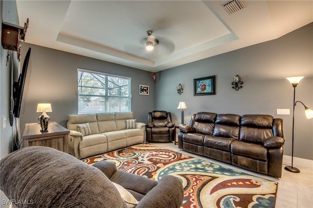 tiled living room with visible vents, a tray ceiling, ceiling fan, and baseboards