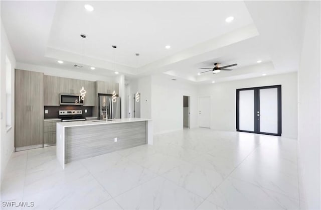 kitchen featuring a tray ceiling, appliances with stainless steel finishes, an island with sink, and hanging light fixtures