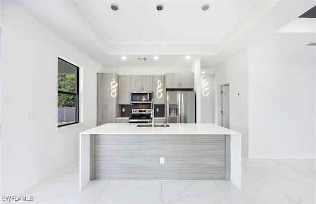 kitchen featuring appliances with stainless steel finishes, hanging light fixtures, a kitchen island with sink, and a tray ceiling