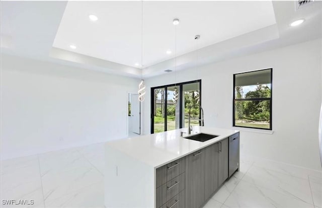 kitchen with sink, a tray ceiling, decorative light fixtures, stainless steel dishwasher, and a kitchen island with sink