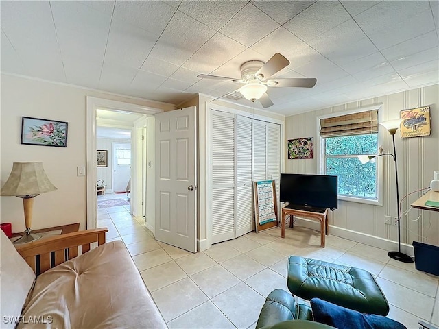 living area with crown molding, light tile patterned flooring, a ceiling fan, and baseboards