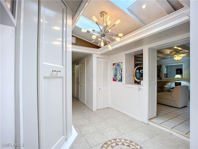 hall with light tile patterned floors, a notable chandelier, baseboards, vaulted ceiling, and ornamental molding