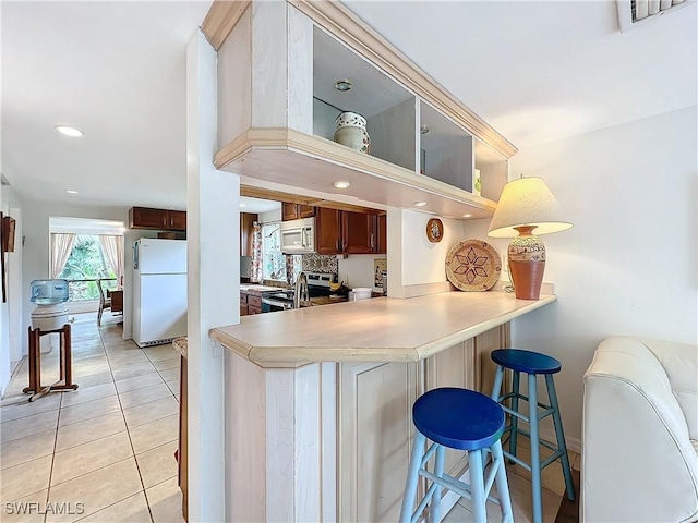 kitchen with visible vents, decorative backsplash, light tile patterned flooring, white appliances, and a peninsula