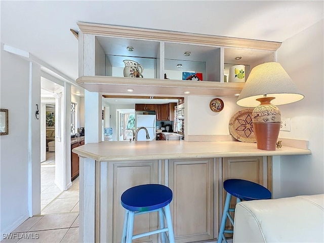 kitchen featuring light tile patterned floors, a kitchen breakfast bar, freestanding refrigerator, a peninsula, and light countertops