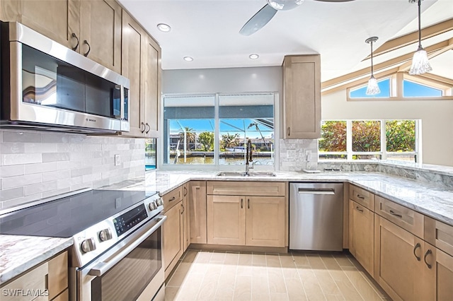 kitchen with decorative light fixtures, stainless steel appliances, light stone counters, and sink