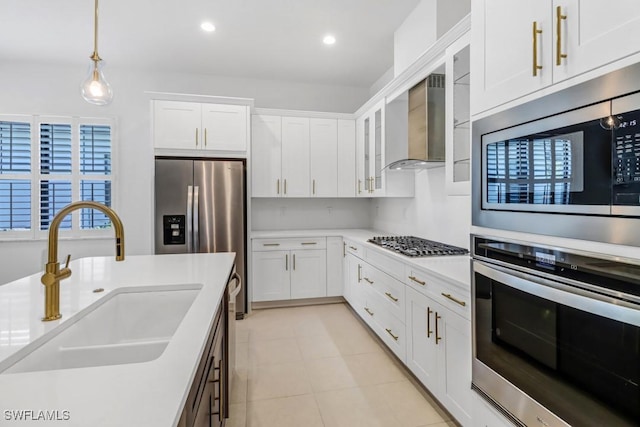 kitchen featuring hanging light fixtures, stainless steel appliances, white cabinets, wall chimney range hood, and sink