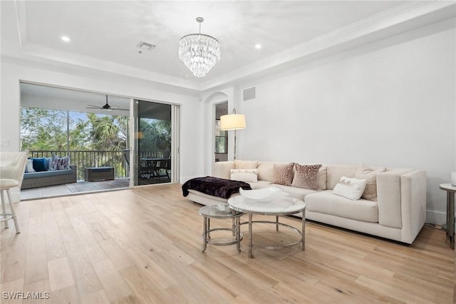 living room featuring light wood-type flooring, ceiling fan with notable chandelier, ornamental molding, and a raised ceiling