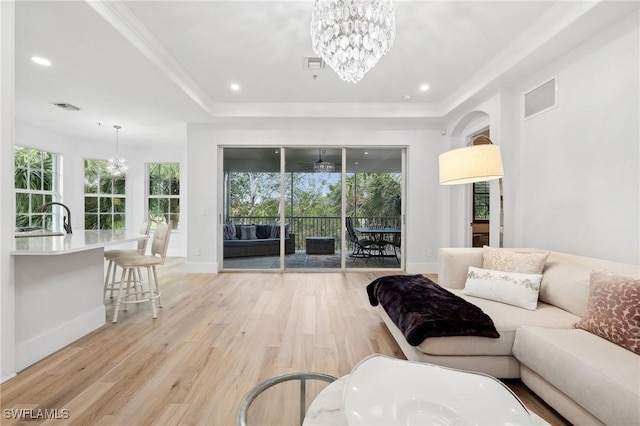 living room with a notable chandelier, ornamental molding, light wood-type flooring, and sink