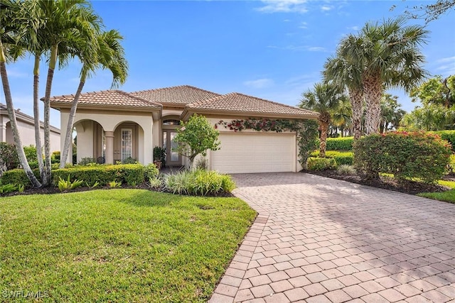 mediterranean / spanish-style home featuring an attached garage, a tile roof, decorative driveway, stucco siding, and a front lawn