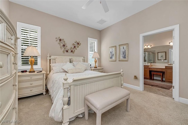 bedroom with ensuite bathroom, light colored carpet, a ceiling fan, baseboards, and visible vents