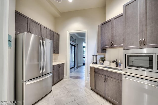 kitchen featuring light countertops, appliances with stainless steel finishes, a sink, and dark brown cabinetry