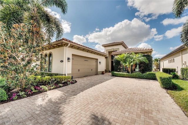 mediterranean / spanish-style house with an attached garage, a tiled roof, decorative driveway, and stucco siding