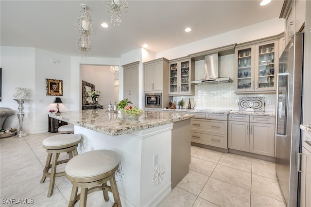 kitchen with stainless steel appliances, light stone counters, wall chimney exhaust hood, and tasteful backsplash