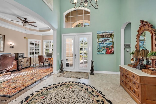 tiled entryway featuring french doors, a high ceiling, ornamental molding, ceiling fan, and a raised ceiling