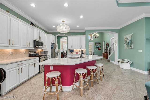 kitchen featuring appliances with stainless steel finishes, decorative backsplash, a breakfast bar, white cabinetry, and a kitchen island with sink