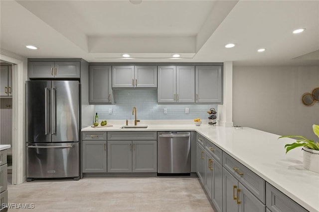 kitchen featuring gray cabinets, appliances with stainless steel finishes, a tray ceiling, and tasteful backsplash