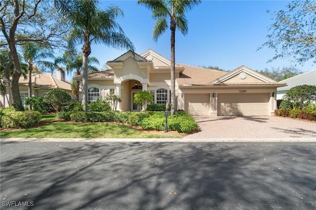 mediterranean / spanish-style home with decorative driveway, a tile roof, an attached garage, and stucco siding