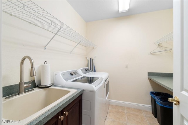 washroom featuring washing machine and clothes dryer, light tile patterned floors, cabinet space, a sink, and baseboards