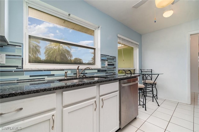 kitchen with dark stone counters, white cabinets, backsplash, stainless steel dishwasher, and a sink