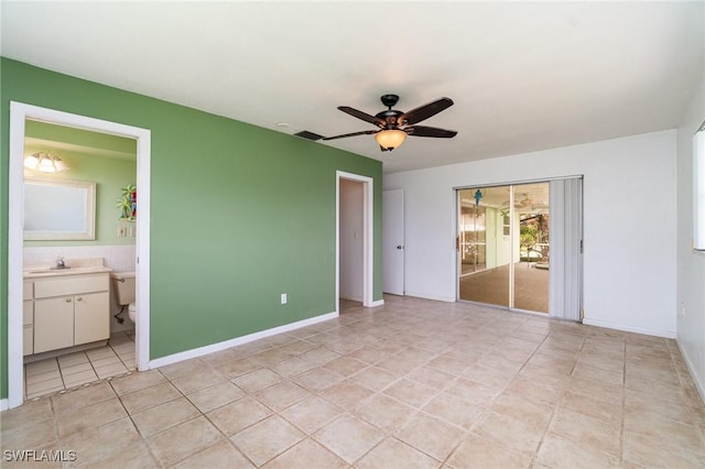 unfurnished bedroom with light tile patterned floors, a sink, ceiling fan, ensuite bath, and baseboards