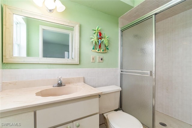 full bath featuring toilet, tiled shower, vanity, and tile walls