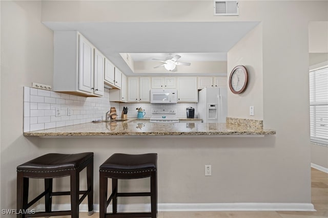 kitchen with white appliances, kitchen peninsula, white cabinets, light stone countertops, and tasteful backsplash