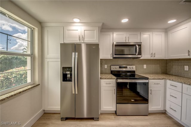 kitchen with tasteful backsplash, stainless steel appliances, white cabinets, light wood finished floors, and light stone countertops