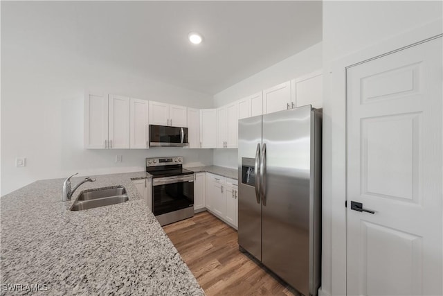 kitchen with light wood-type flooring, stainless steel appliances, light stone countertops, sink, and white cabinets