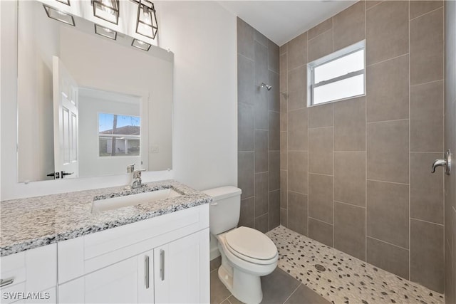 bathroom with vanity, tile patterned flooring, tiled shower, and toilet