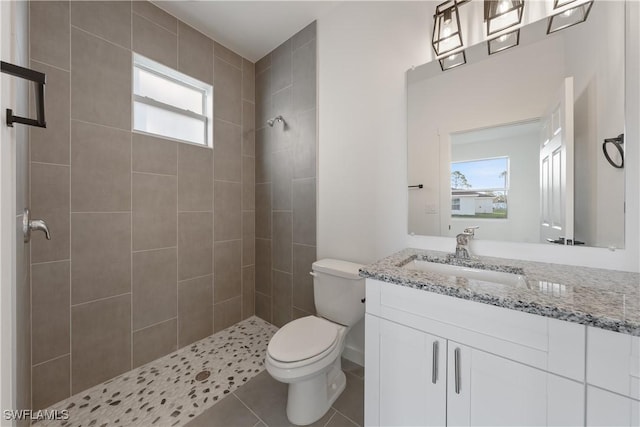 bathroom featuring vanity, a tile shower, toilet, and tile patterned floors