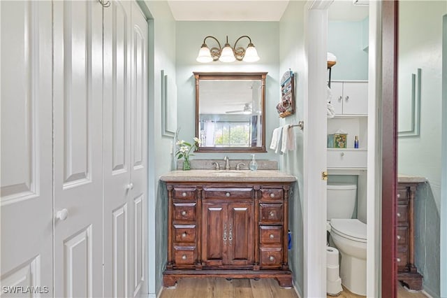 bathroom with a ceiling fan, toilet, wood finished floors, vanity, and a closet