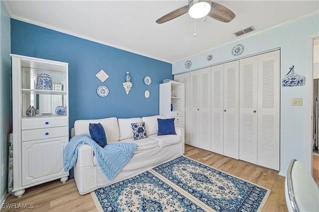 living room featuring a ceiling fan, visible vents, crown molding, and wood finished floors