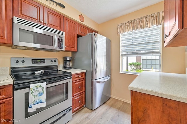 kitchen with light wood finished floors, baseboards, appliances with stainless steel finishes, and light countertops