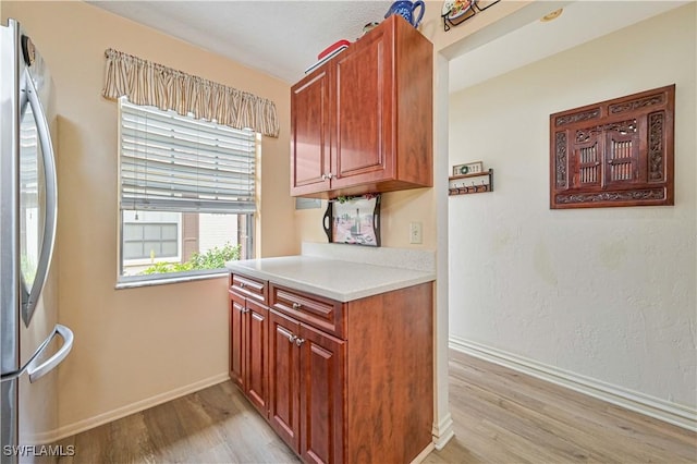 kitchen featuring light countertops, light wood-style flooring, baseboards, and stainless steel refrigerator