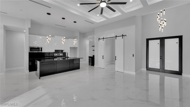 kitchen with pendant lighting, a barn door, white cabinetry, stainless steel microwave, and an island with sink