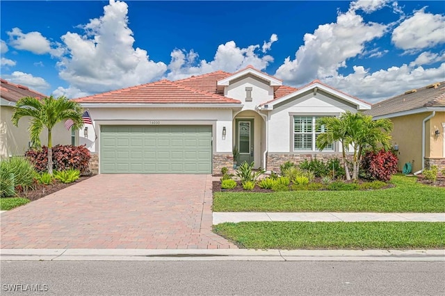 view of front facade featuring stone siding, a tile roof, an attached garage, decorative driveway, and stucco siding