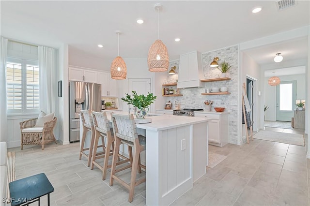 kitchen with open shelves, light countertops, a kitchen island with sink, white cabinets, and stainless steel fridge