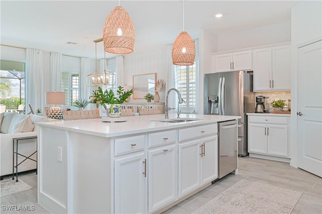 kitchen with a sink, hanging light fixtures, appliances with stainless steel finishes, light countertops, and an island with sink