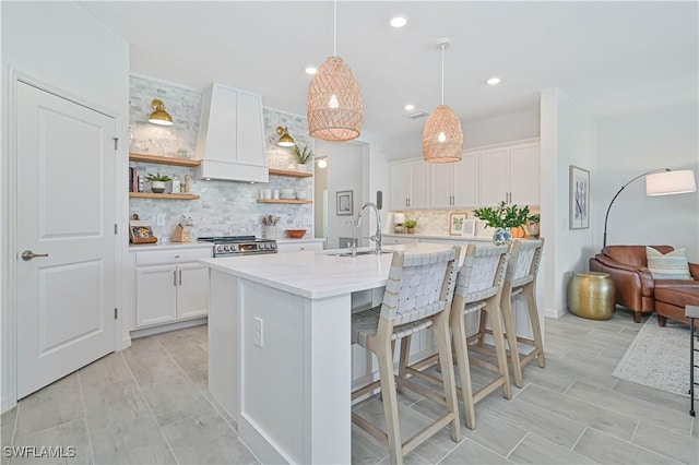 kitchen featuring a center island with sink, pendant lighting, white cabinetry, open shelves, and a sink